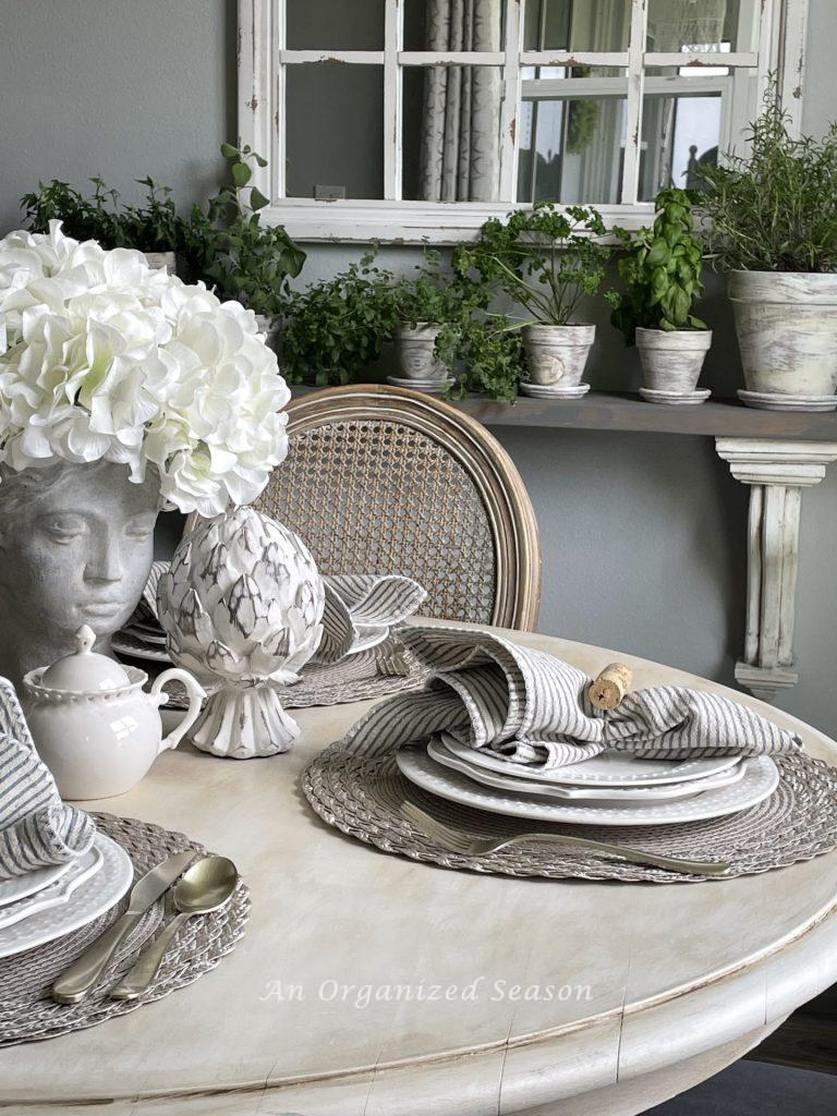 Kitchen table with place settings and a shelf with herbs in pots. 