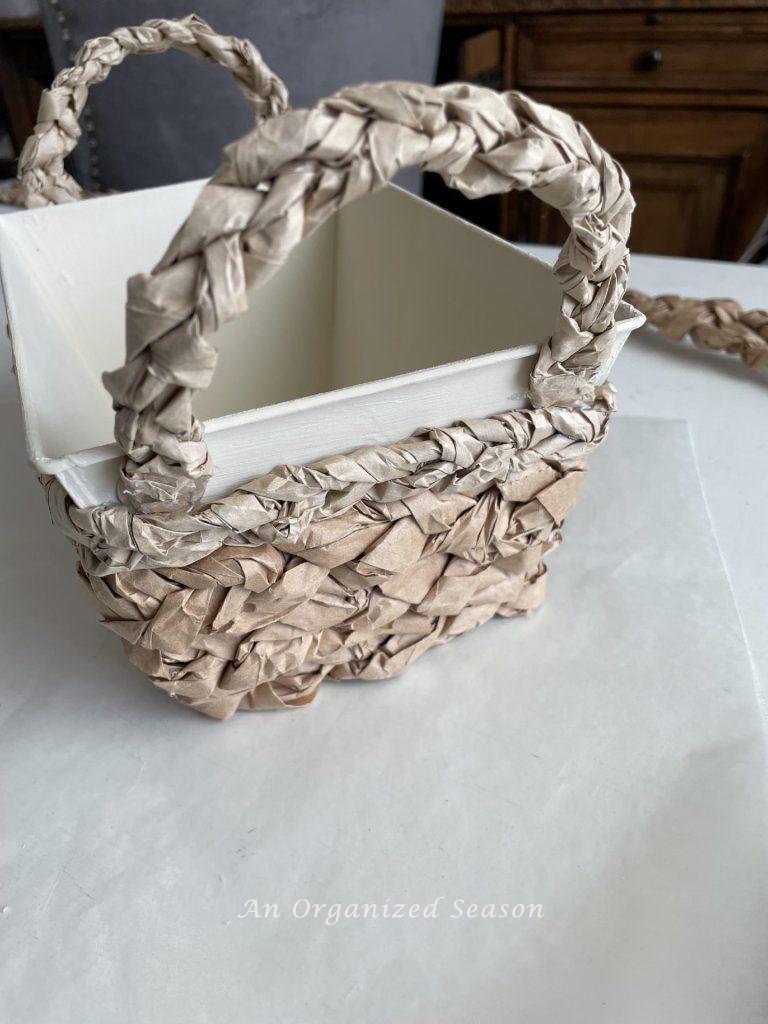 Step ten to make a packing paper basket is to adhere the handles to the base.
