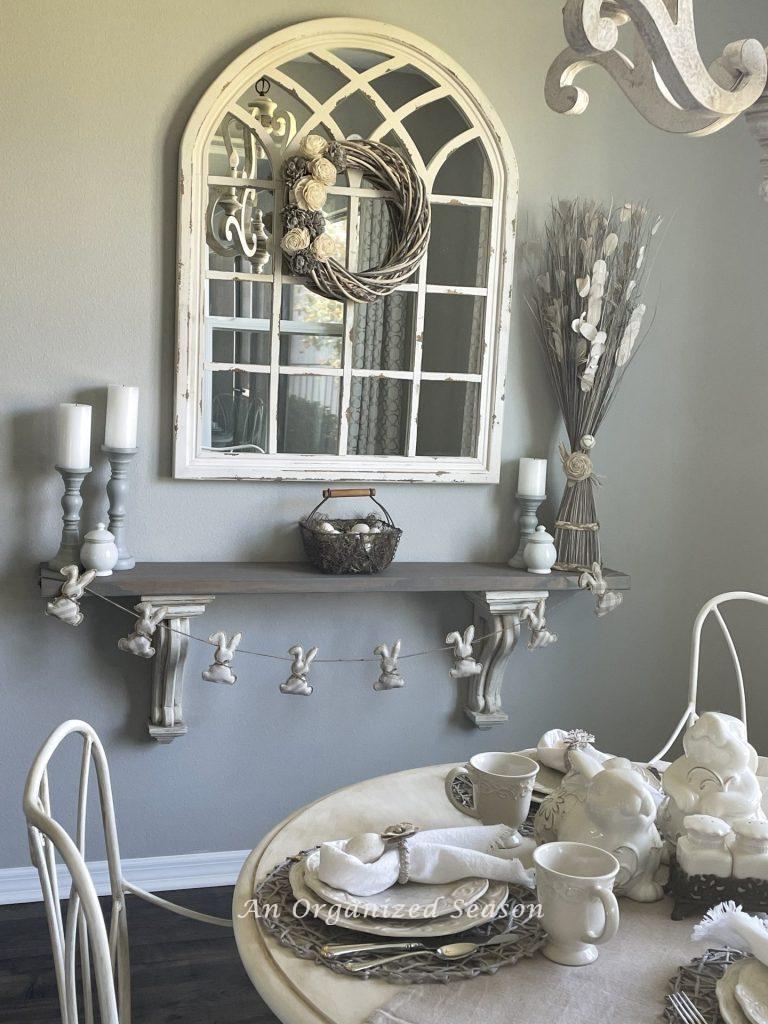 A white mirror hanging over a shelf with corbels that decorated for Easter. 