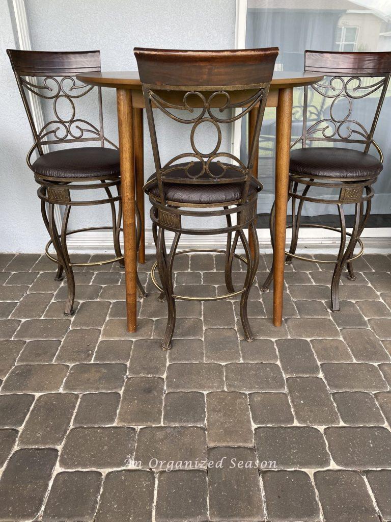 A brown table and stools sitting on a brick patio. 