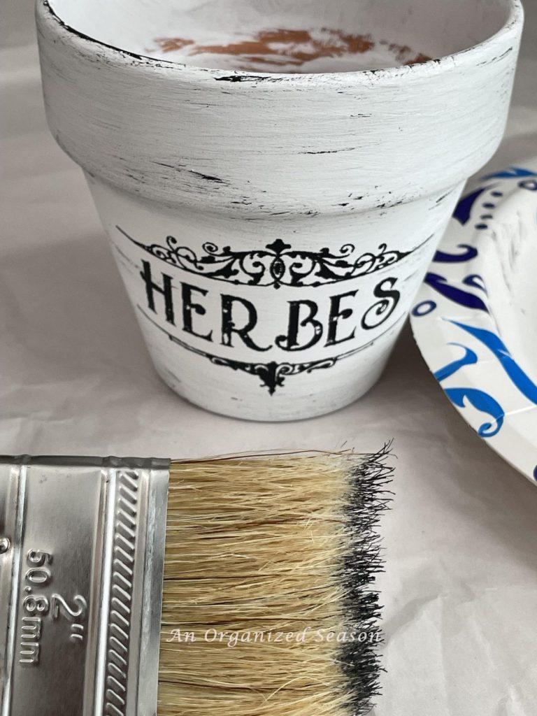 Step three to paint flower pots is to distress them with black paint and a chip brush.