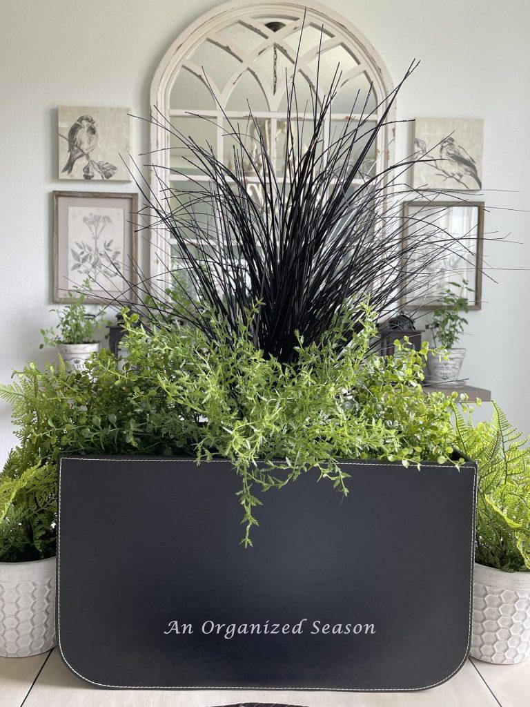 Centerpiece with black leather container filled with greenery and black faux grass are table decor for Father's Day.
