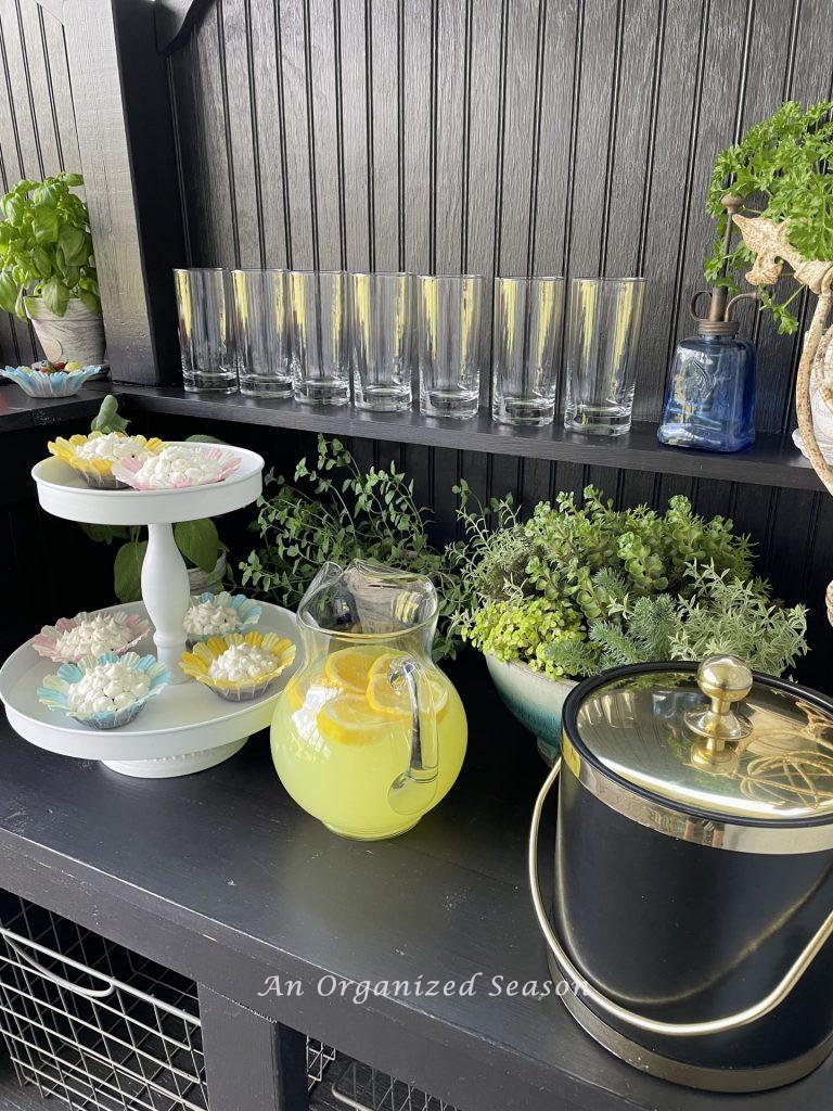 A potting bench with tiered tray of cupcakes and a pitcher of lemonade. 