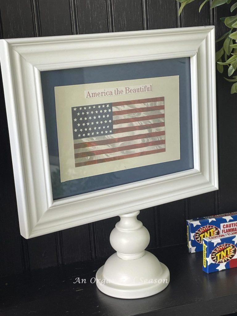 White picture frame on a stand with a picture of American flag. 