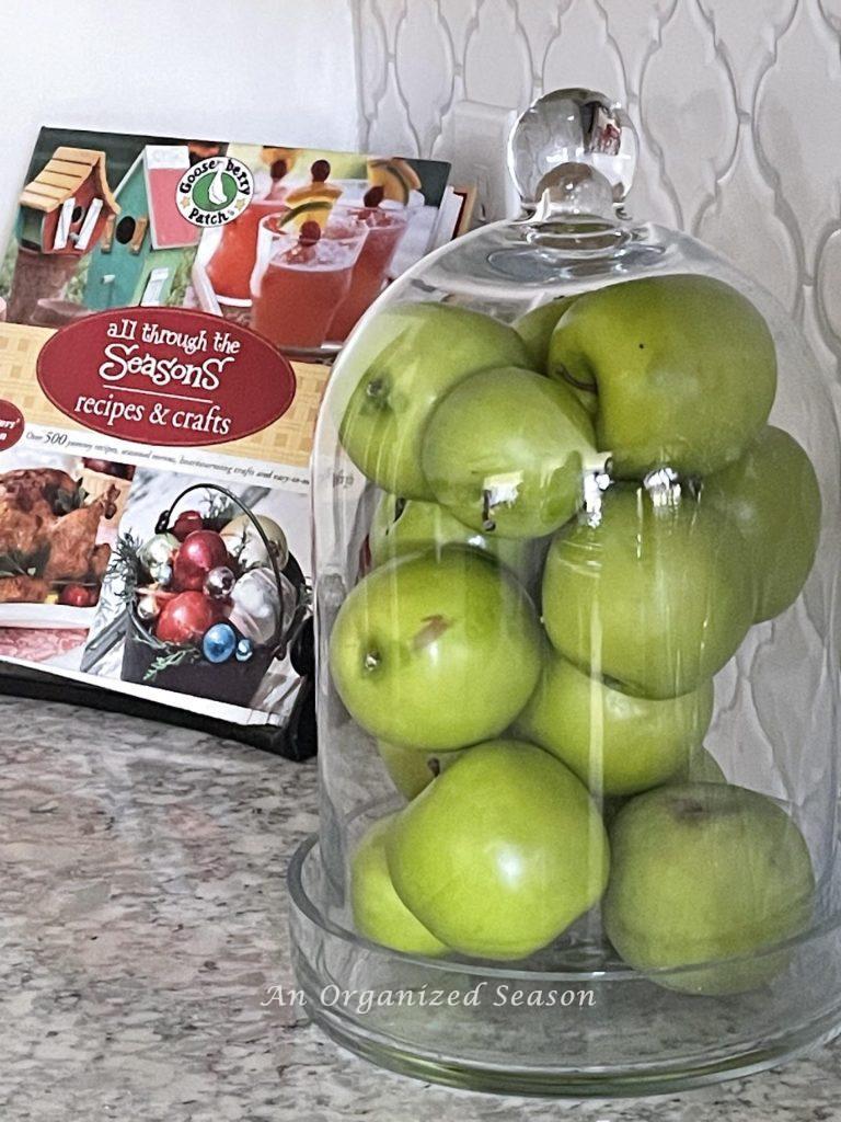 Summer decor tip #2, Display green apples in a glass cloche on a kitchen counter.
