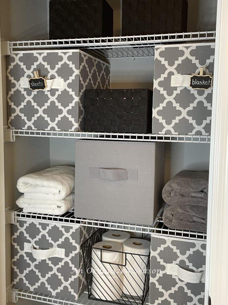 An bathroom closet organized with gray bins. 