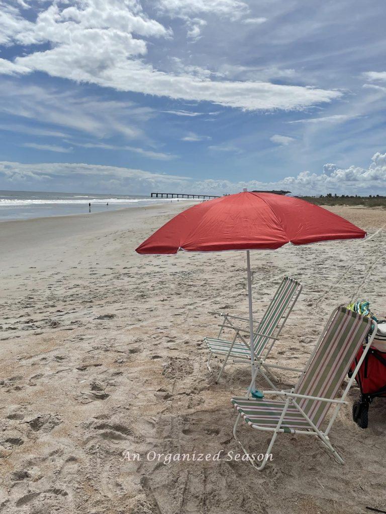 A red umbrella and two chairs on a beach.