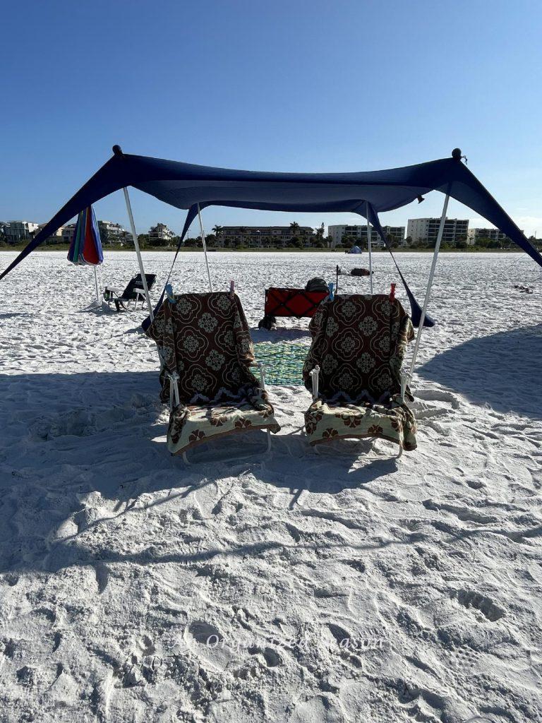 A tent, two chairs, blanket, and wagon set up on a beach are essential things to pack. 