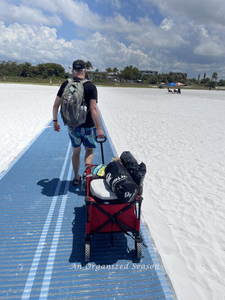 A man pulling a wagon filled with beach items down a beach access walk. 