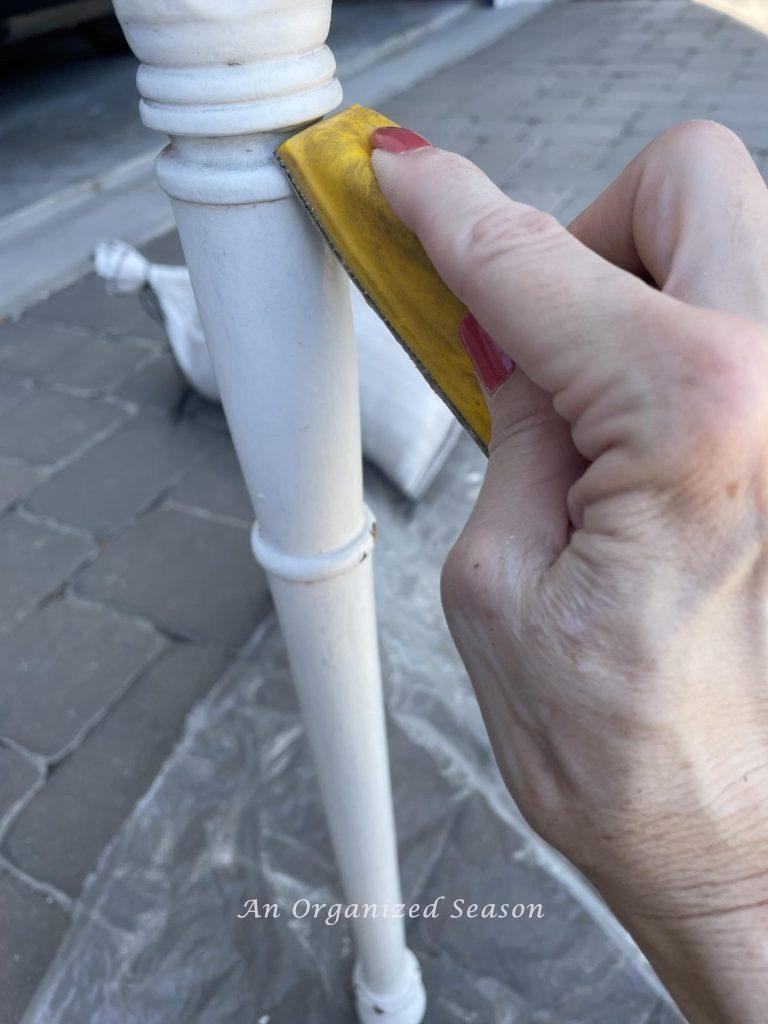 A woman using a small sanding tool on the leg of a desk. 