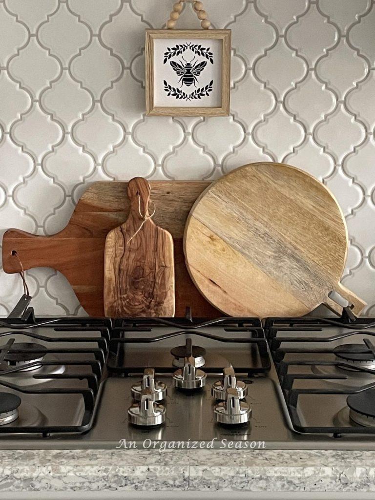 Three wooden cutting boards displayed behind a stove with a small bee picture hanging above them. 