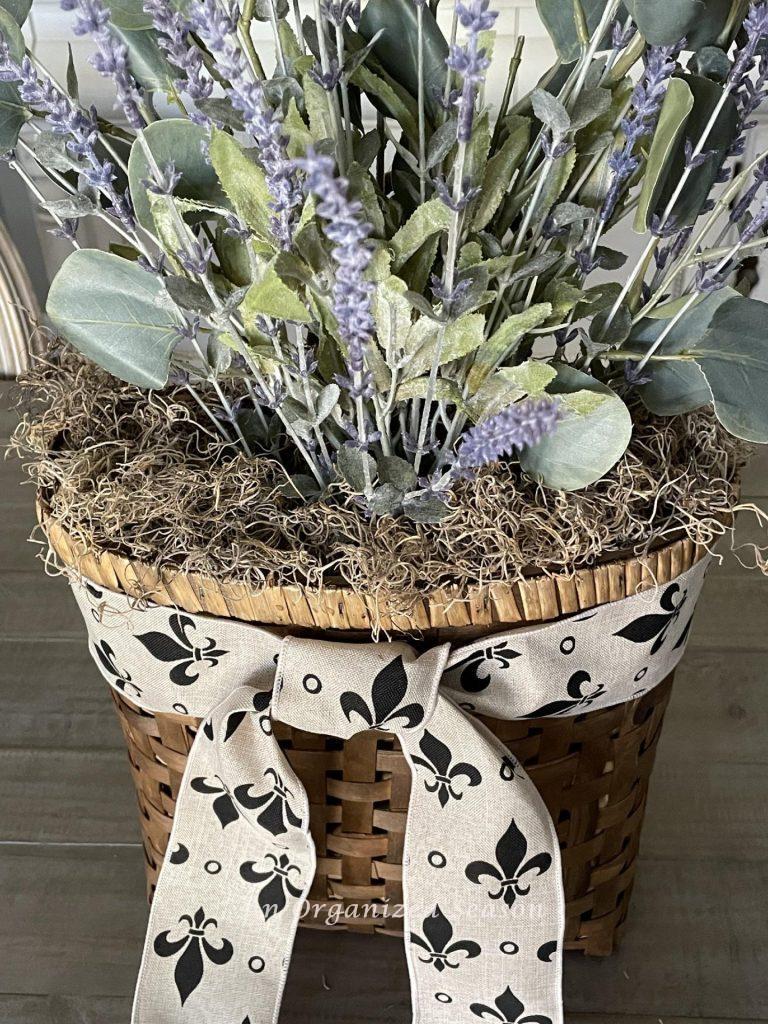 A ribbon with fleur di lis wrapped around a basket of lavender.