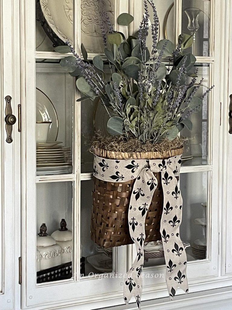 A basket of lavender and eucalyptus hanging on a china cabinet. 