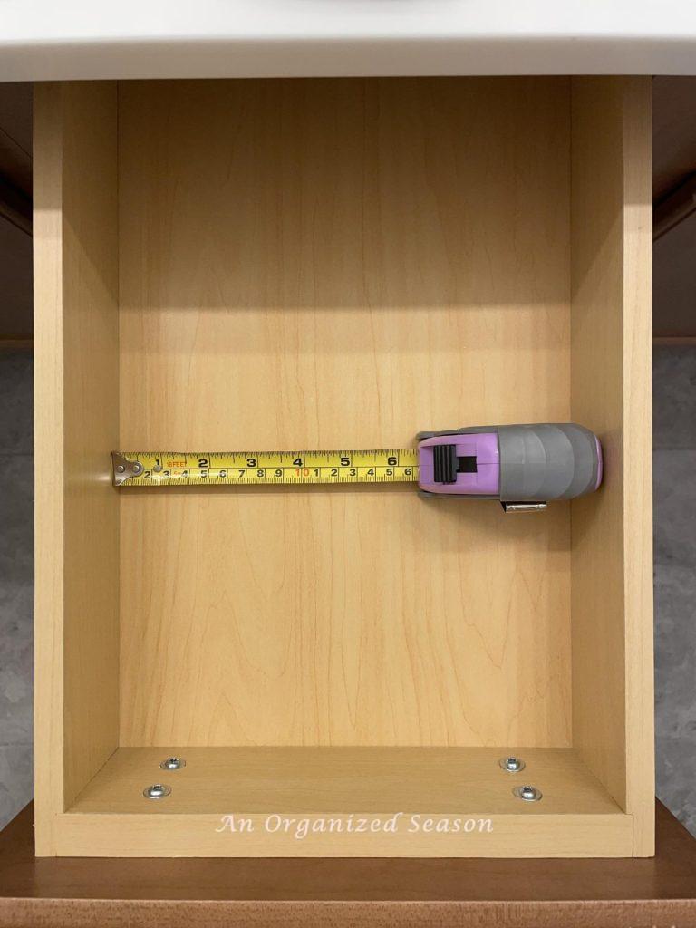 A tape measure inside a bathroom drawer to determine what organizing container will fit.