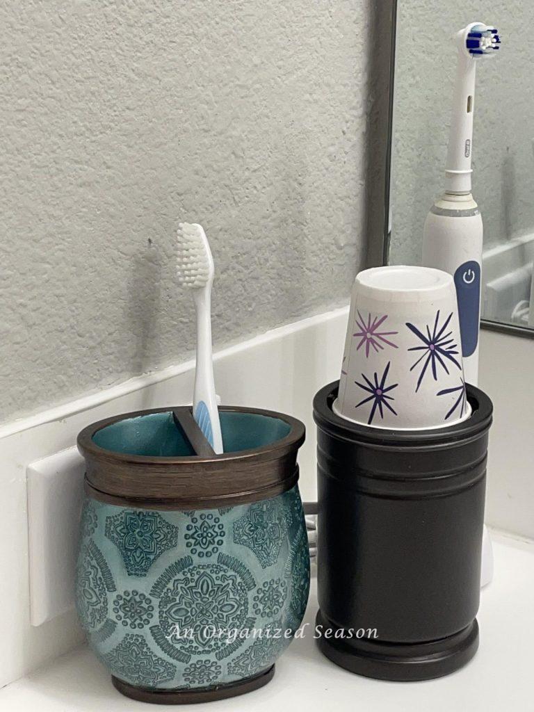 Electric toothbrush, cup holder, and toothbrush holder on a bathroom counter. 