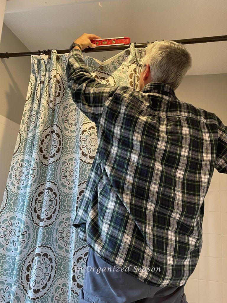 A man checking to see of a shower curtain rod is level in a bathroom.