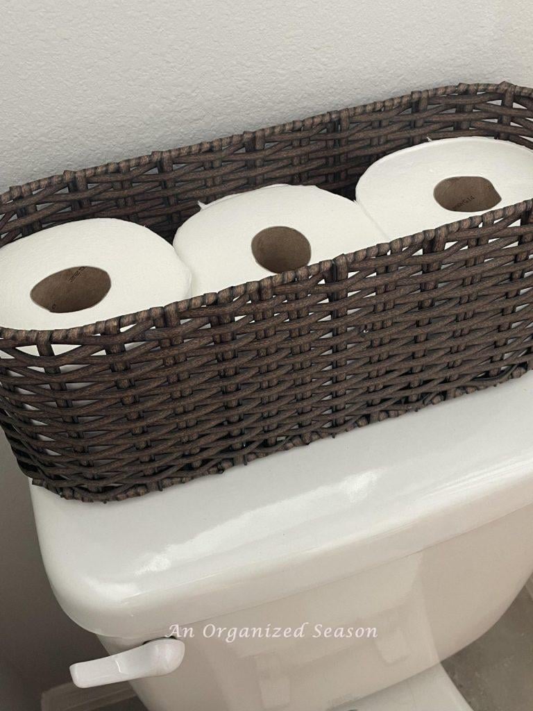 Toilet paper in a basket on the back of a toilet.