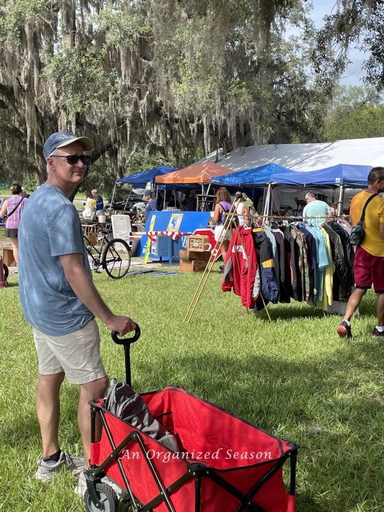 A man and his red wagon at a yard sale. 