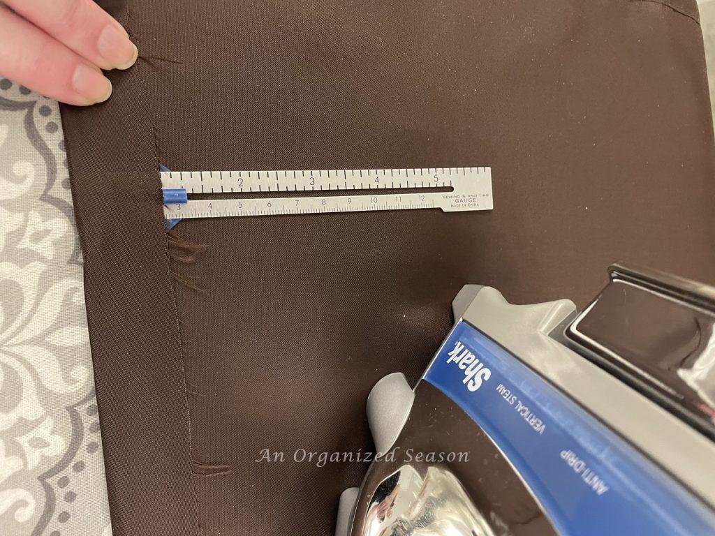 Someone measuring a one inch fold in a piece of brown fabric. 