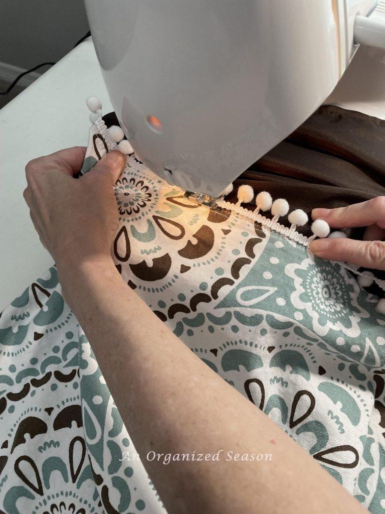 Someone sewing pompom trim on a curtain with a sewing machine. 