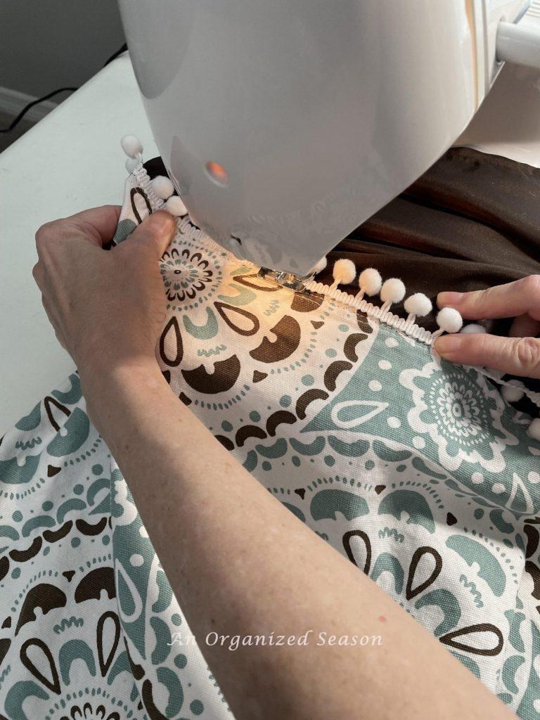 Someone sewing pompom trim on a curtain with a sewing machine.