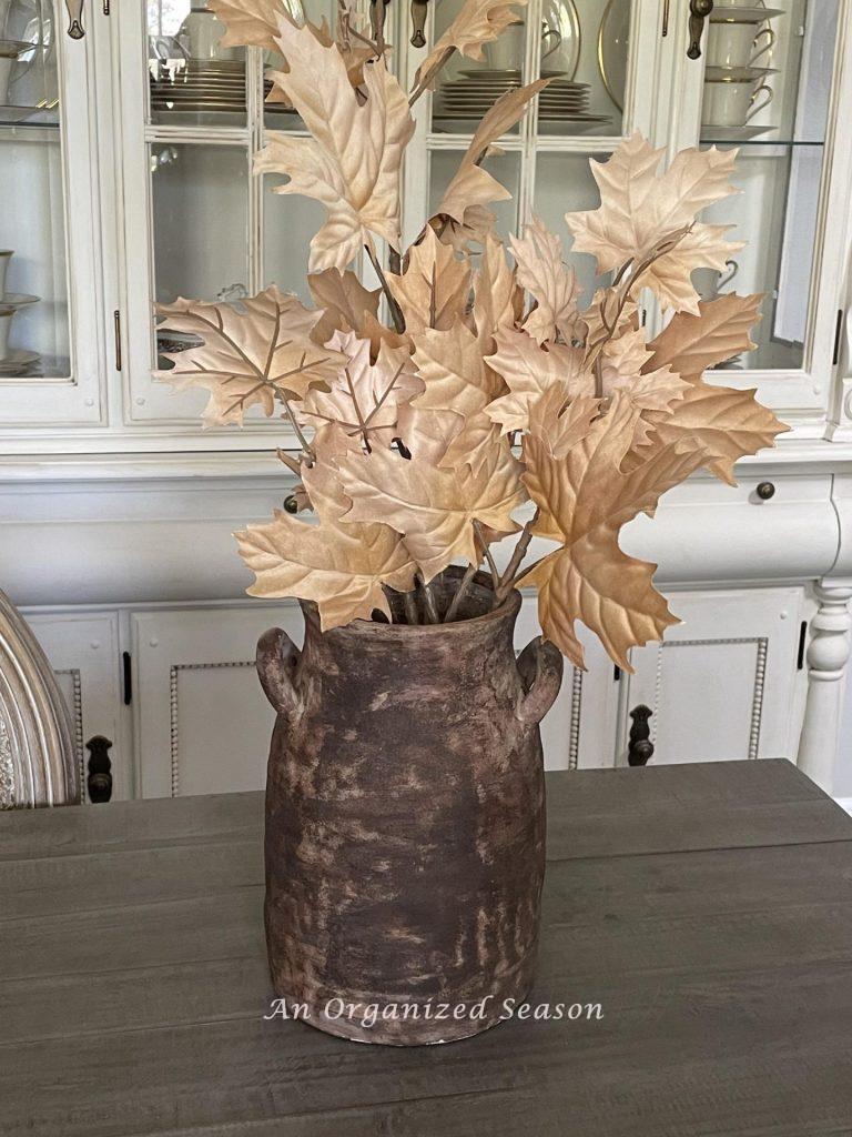 A brown ceramic vase holding branches with tan leaves.