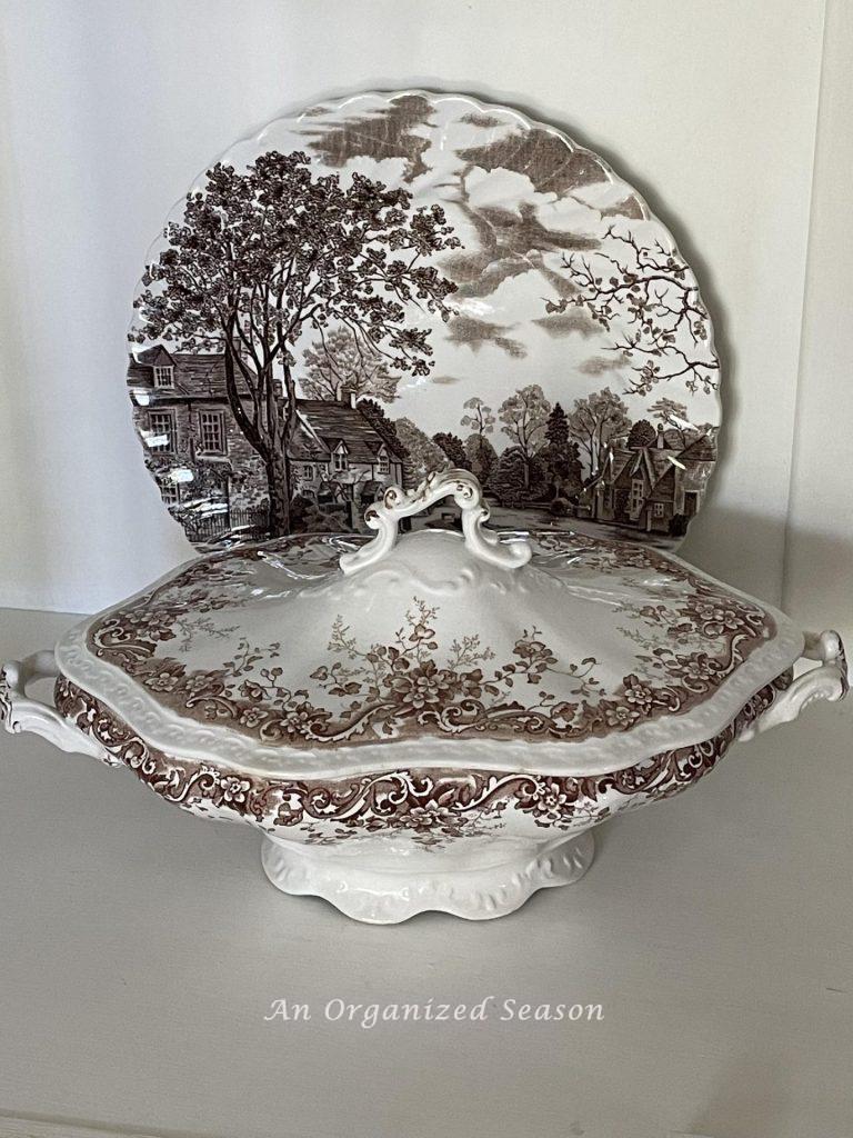 A brown transferware lidded tureen in front of a plate. 