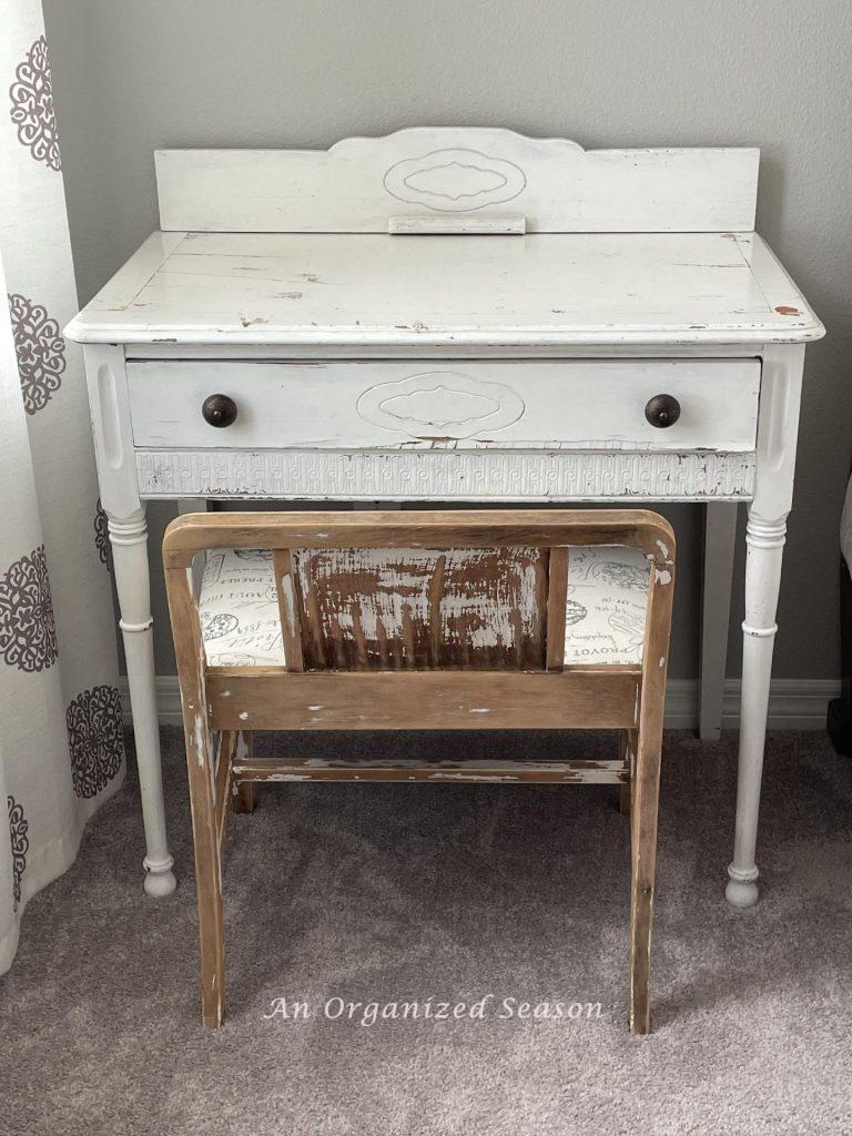 A white desk and stool with peeling paint. 