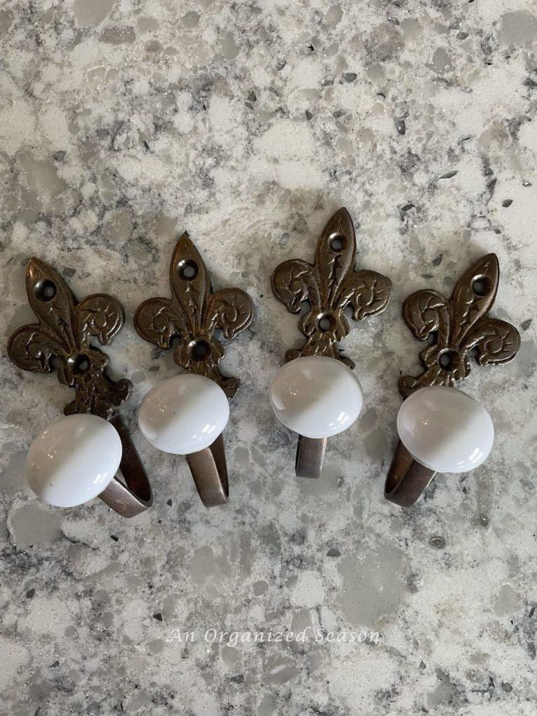 Four brass fleur di lis towel hooks with white knobs. 