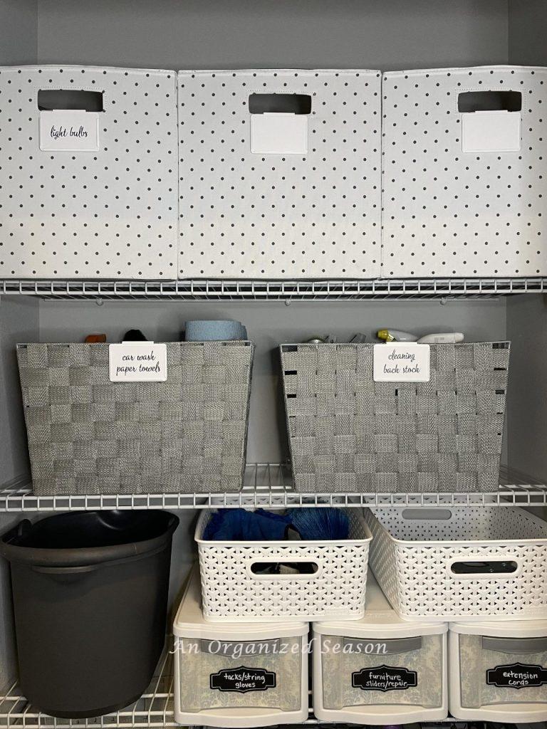 A cleaning closet organized with assorted gray and white bins.