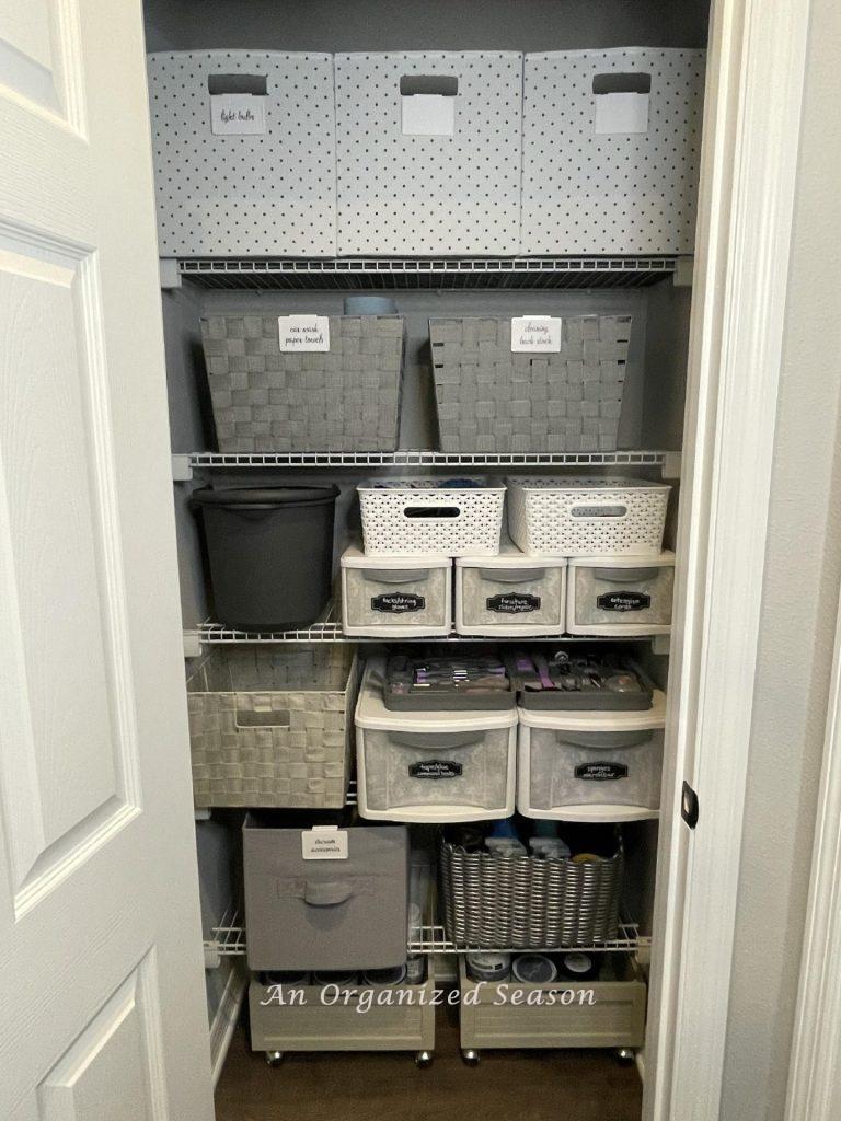 An organized cleaning closet using an assortment of gray and white storage containers. 