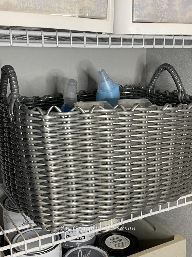 A gray basket stores household cleaning products in a closet.  
