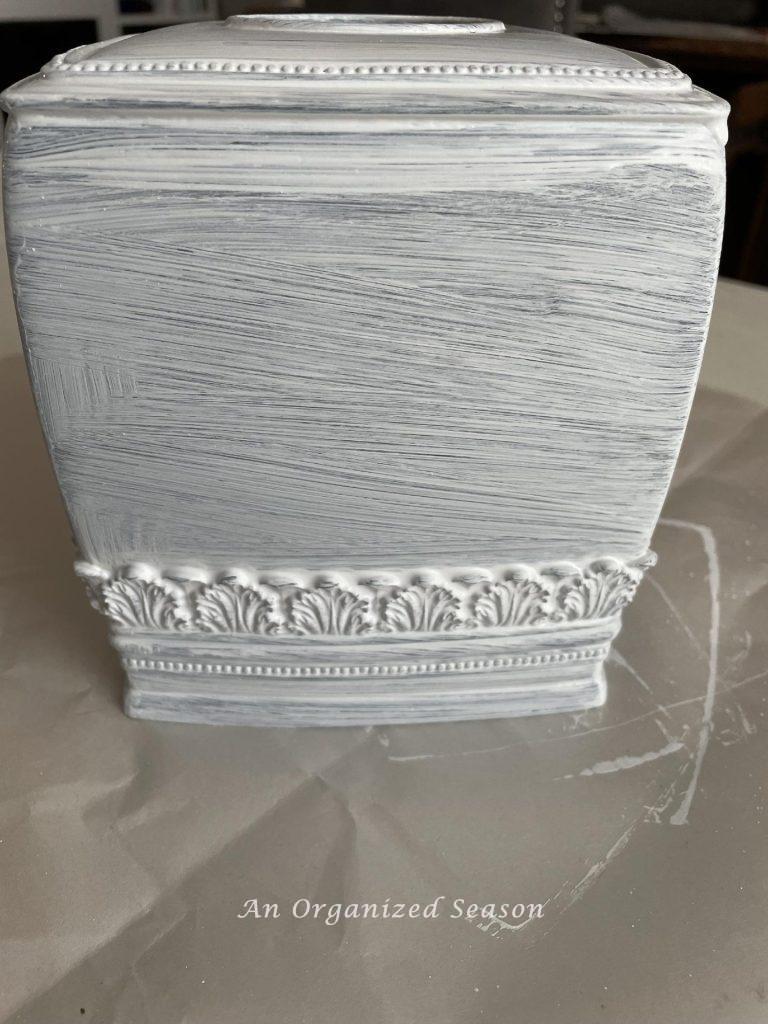 Step one to distress with paint is to add a coat of white paint to a tissue box.