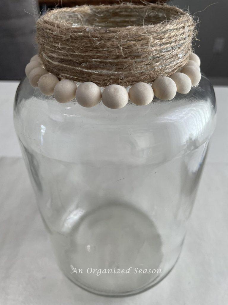 A pickle jar with twine and wood beads covering the top. 
