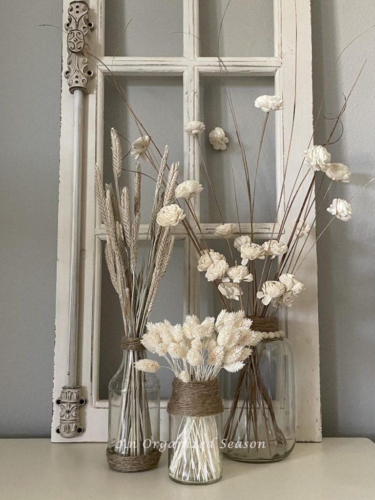 Three twine wrapped vases with neutral dried flowers.