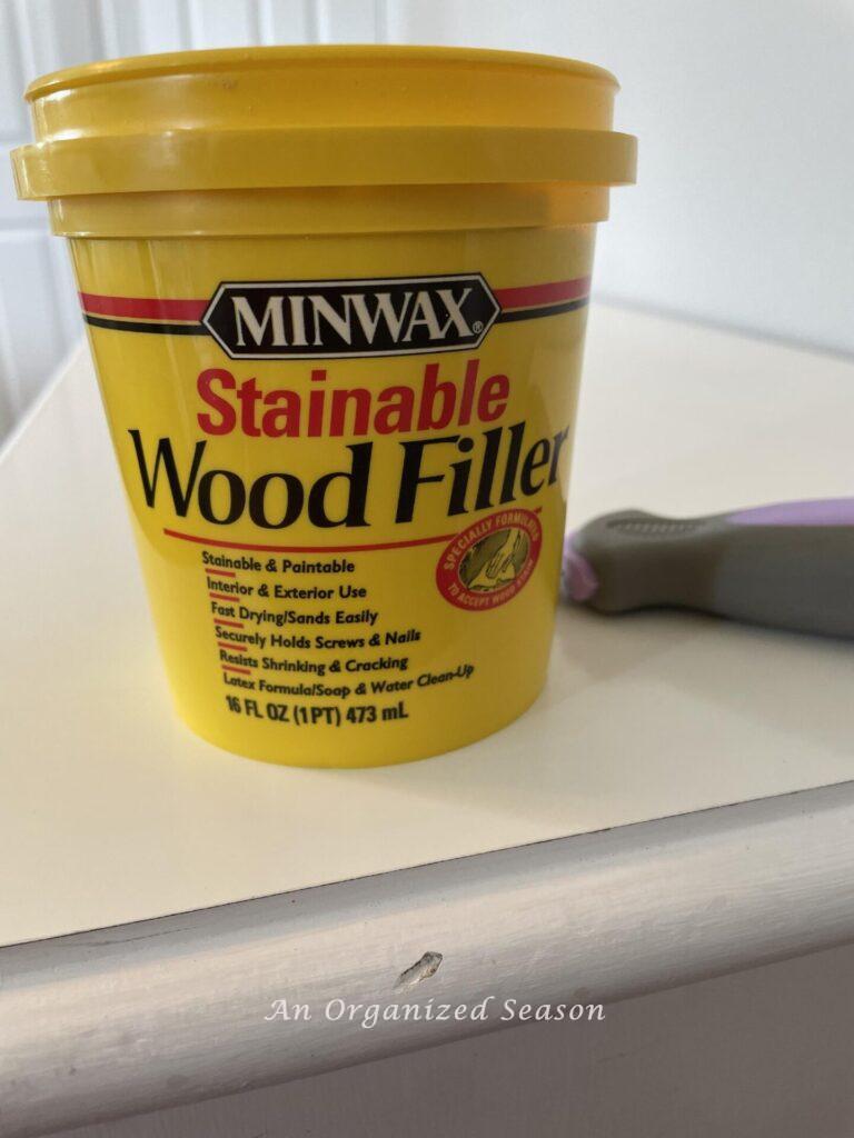 A container of wood filler sitting on a dresser with a small dent. 