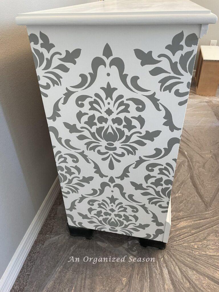 Gray damask design stenciled on the side of a white dresser. 