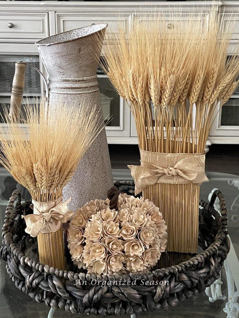 Fall DIY craft #3 are dried wheat bundles in a basket with a pitcher and faux pumpkin. 