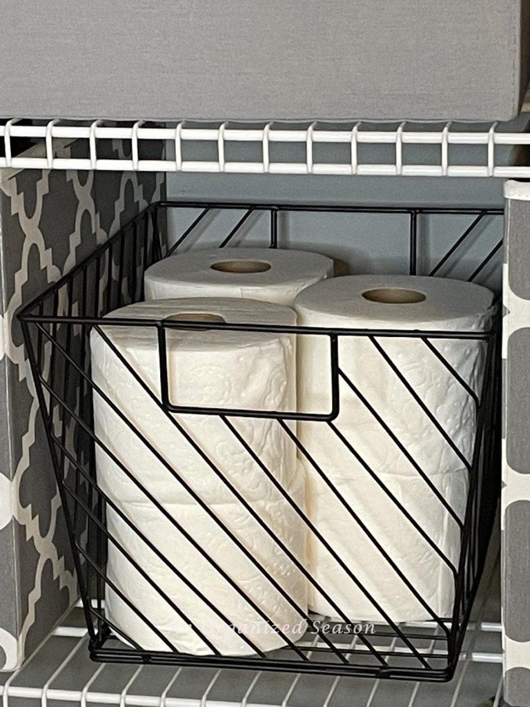Toilet paper rolls stored in a black wire basket. 
