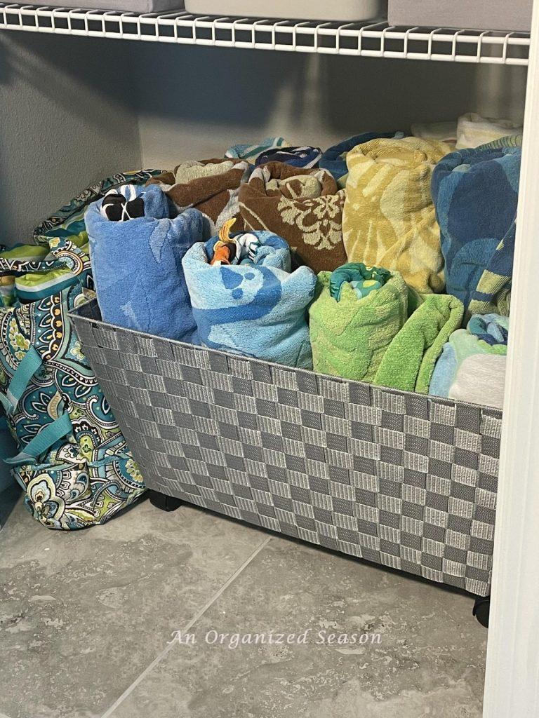 Beach towels rolled and stored in a large basket with wheels inside a closet. 