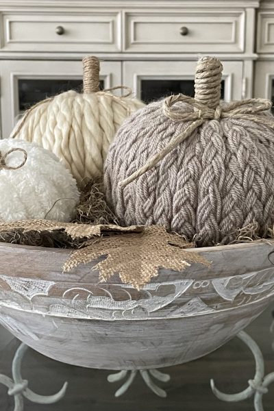 Three DIY yarn pumpkins in a wooden bowl.