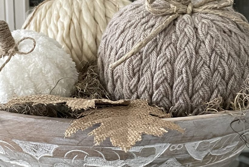 Three DIY yarn pumpkins in a wooden bowl.