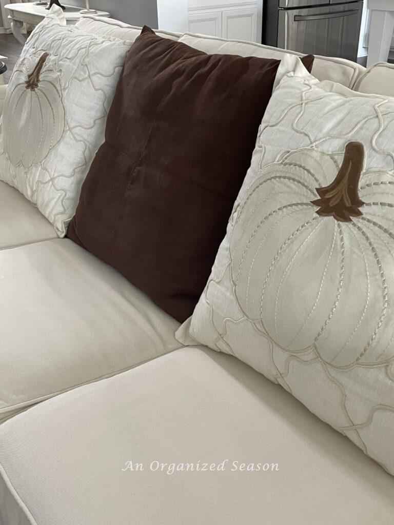 Two pumpkin pillows with a brown pillow in between.