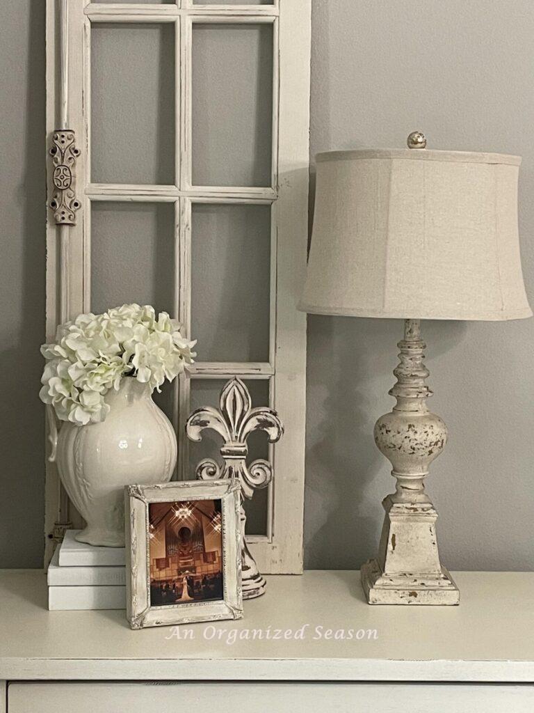 A lamp, picture, floral arrangement, and sculpture on a nightstand. 