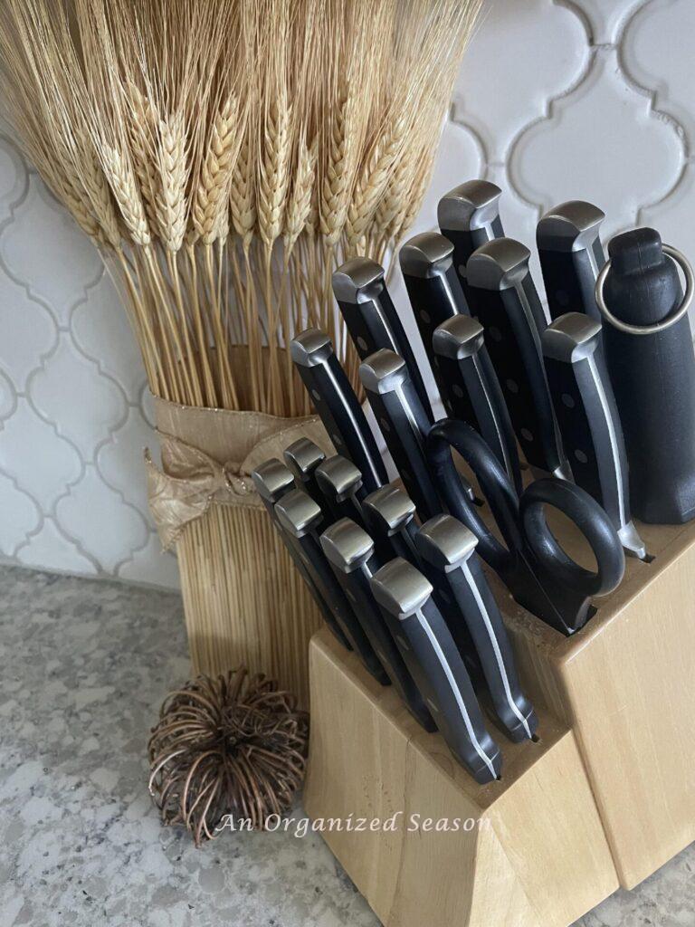 Fall kitchen decor idea #3 is to set a dried wheat arrangement next to a wood knife block and a grapevine pumpkin. 