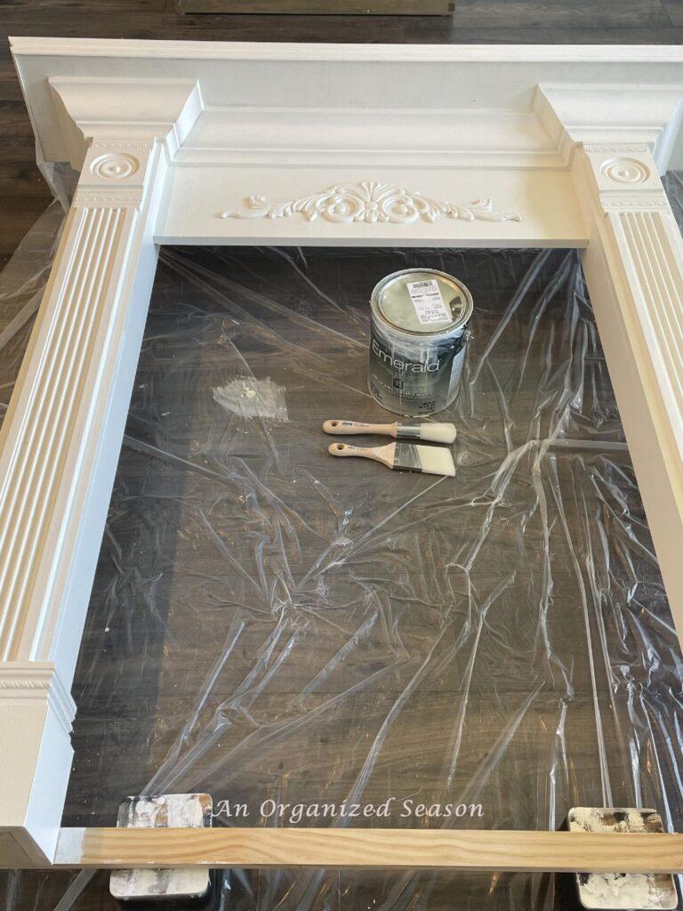 Primed mantel lying on plastic tarp near can of paint and brushes