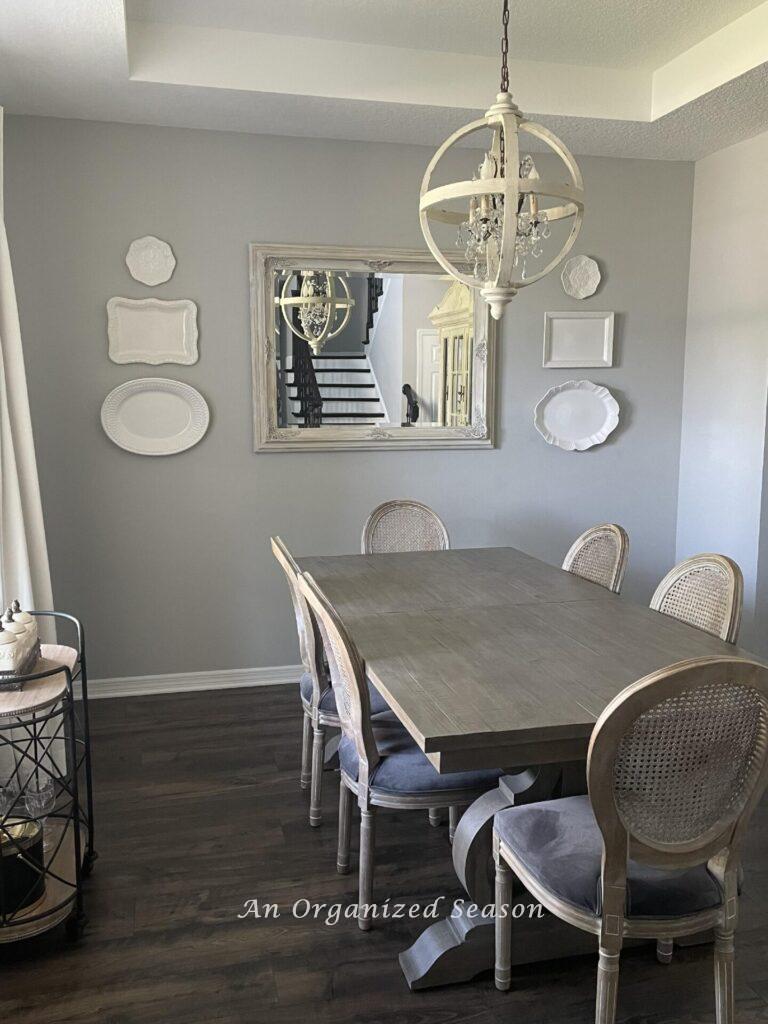 A dining room with six white platters hanging on either side of a mirror. 
