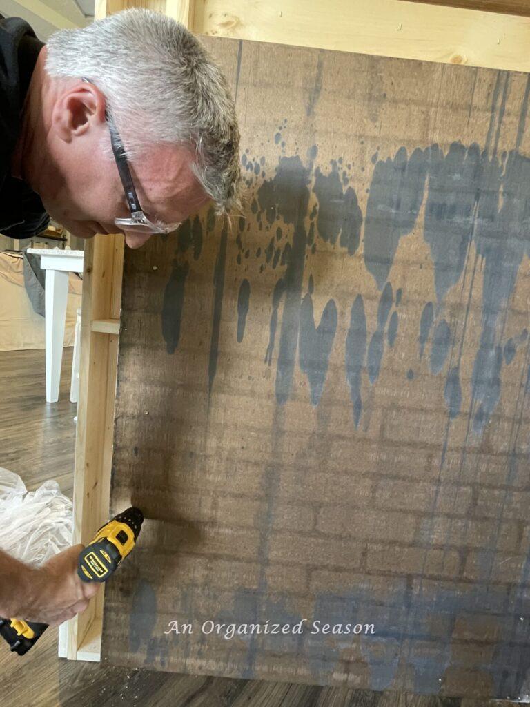 Man putting screws into faux brick sheet to connect to mantel