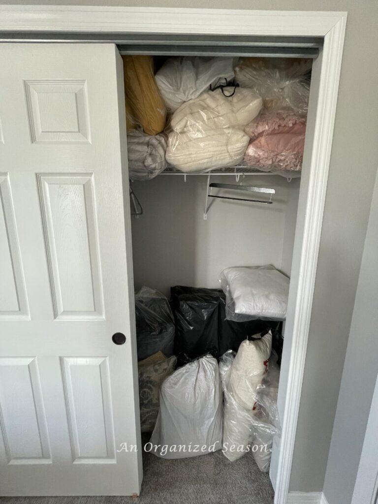 A messy closet filled with clear bags of pillows. 