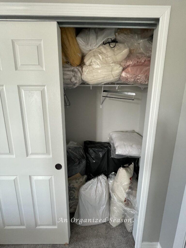 A messy closet filled with clear bags of pillows.